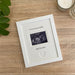White picture frame laying down on the table top next to a white candle and plant, frame is displaying a sonogram scan image for a new Daddy saying 'I'm on my way Daddy with your custom personalisation.