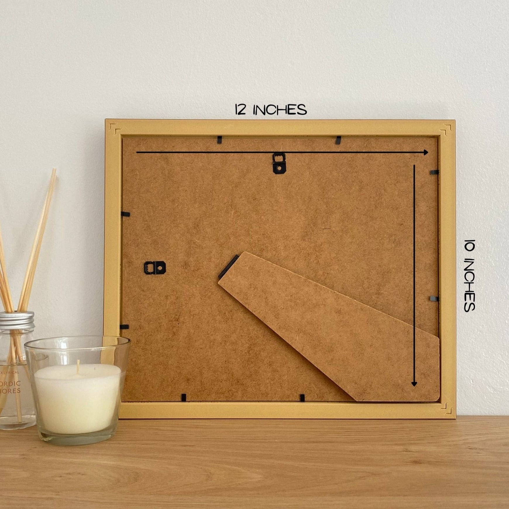 Back of a picture frame on shelf next to a white candle and diffuser