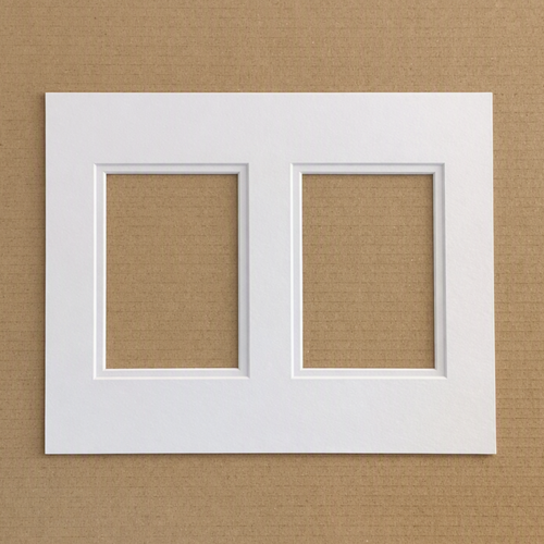A white double-frame mat board or picture frame mat with two rectangular recessed openings, shown flat against a brown textured background.
