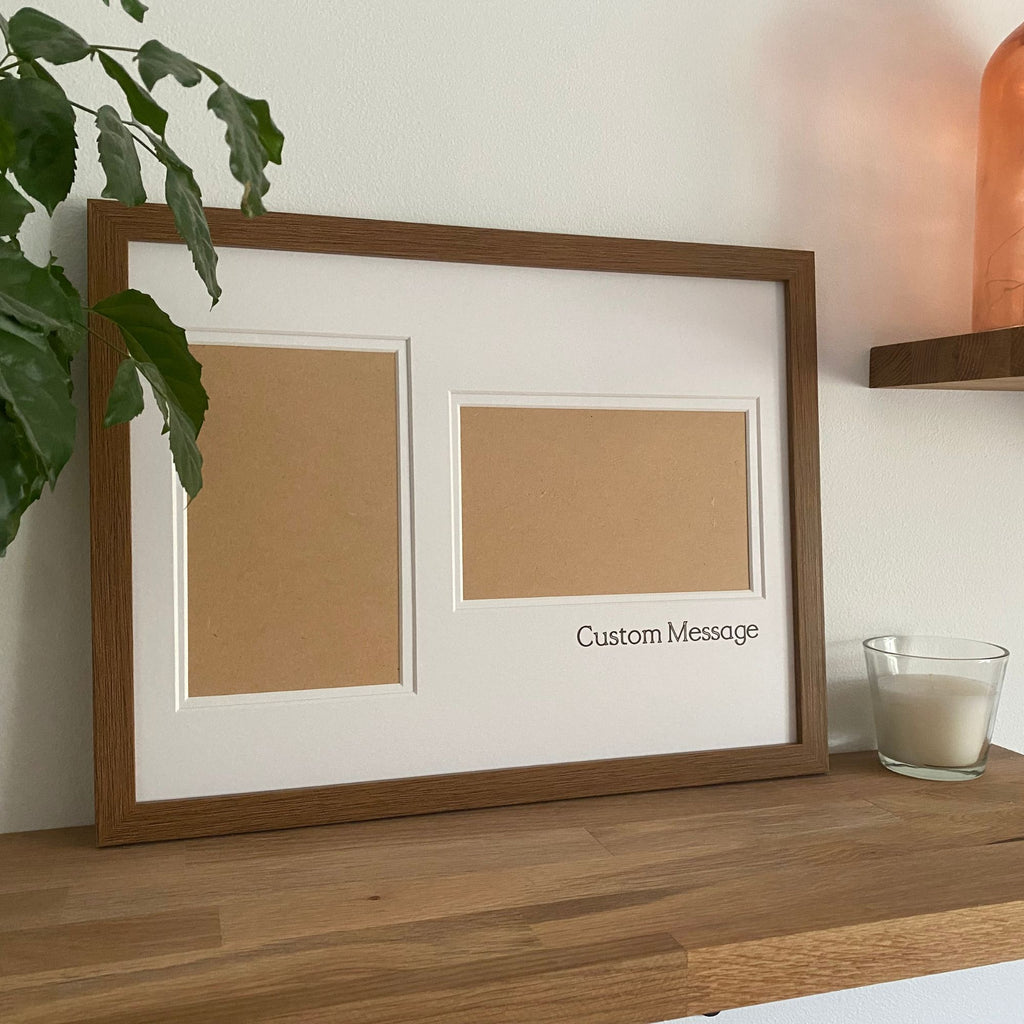 Large brown picture frame standing on the wooden shelf next to a white candle and green leafy plant againt a white wall and rosy pink glass vase