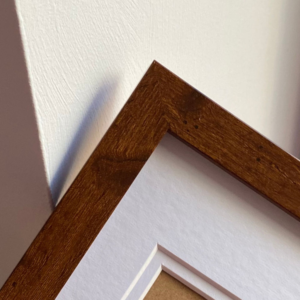 Contemporary, modern teak picture frame with whiote double mount against a white wall.