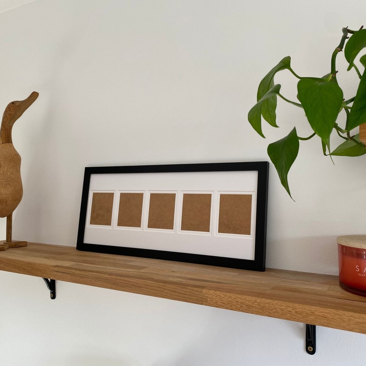 Wooden shelf with a framed picture, plant, and decorative items against a white wall.