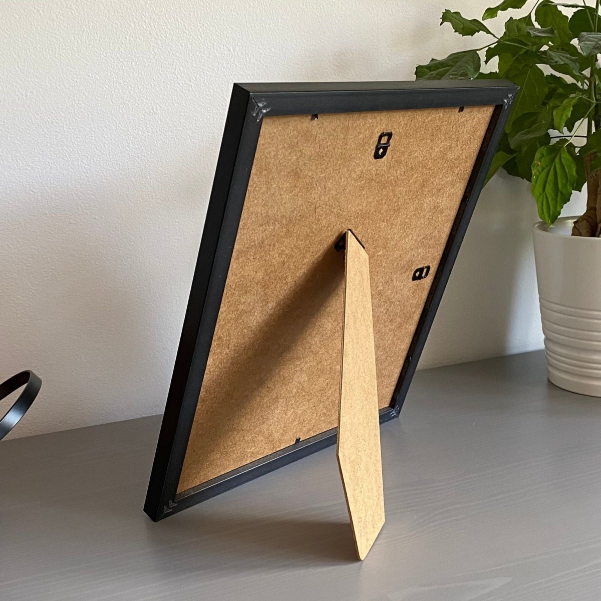 Black photo frame with a strut back on a light surface next to a plant