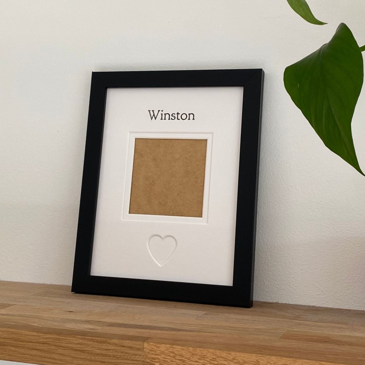Black framed photo display with a heart cutout on a wooden surface.