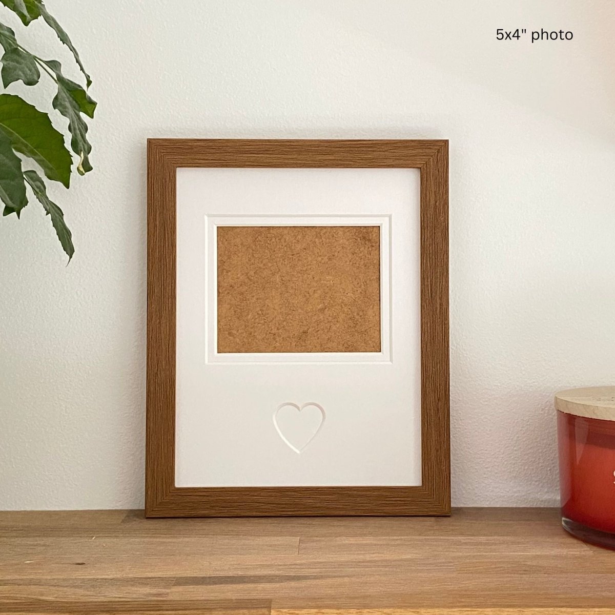 Dark brown photo frame with heart-shaped insert on a wooden surface.