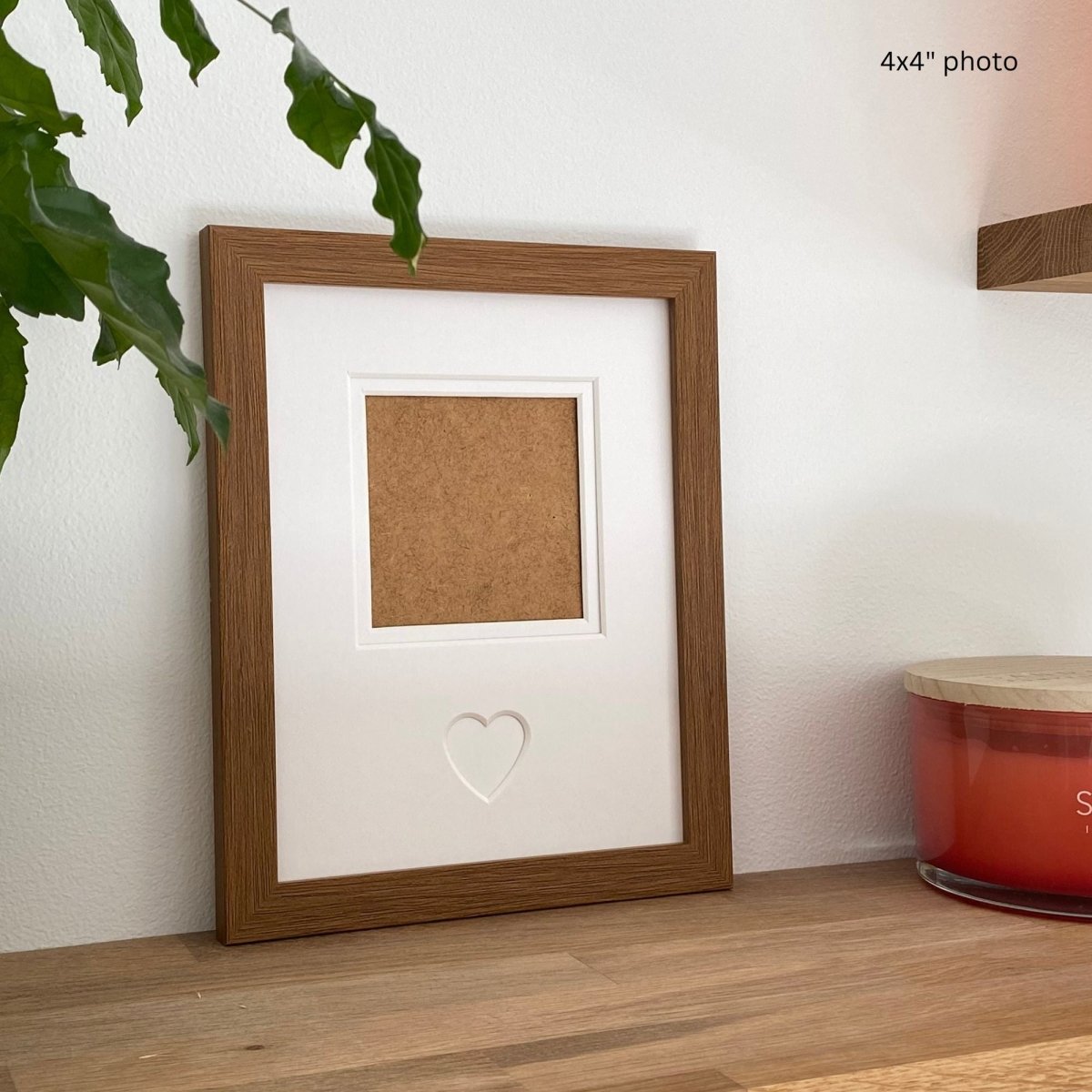 Wooden picture frame on a wooden surface with a plant and candle in the background.