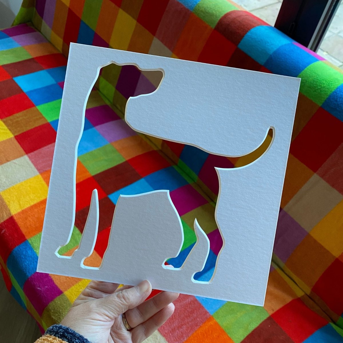 Hand holding a cut-out of a dog silhouette against a colourful checkered background