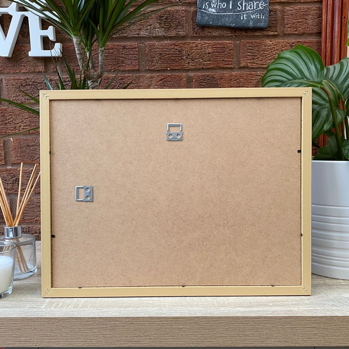 Back of 16x12 frame on shelf next to plant pot and diffuser, candle.