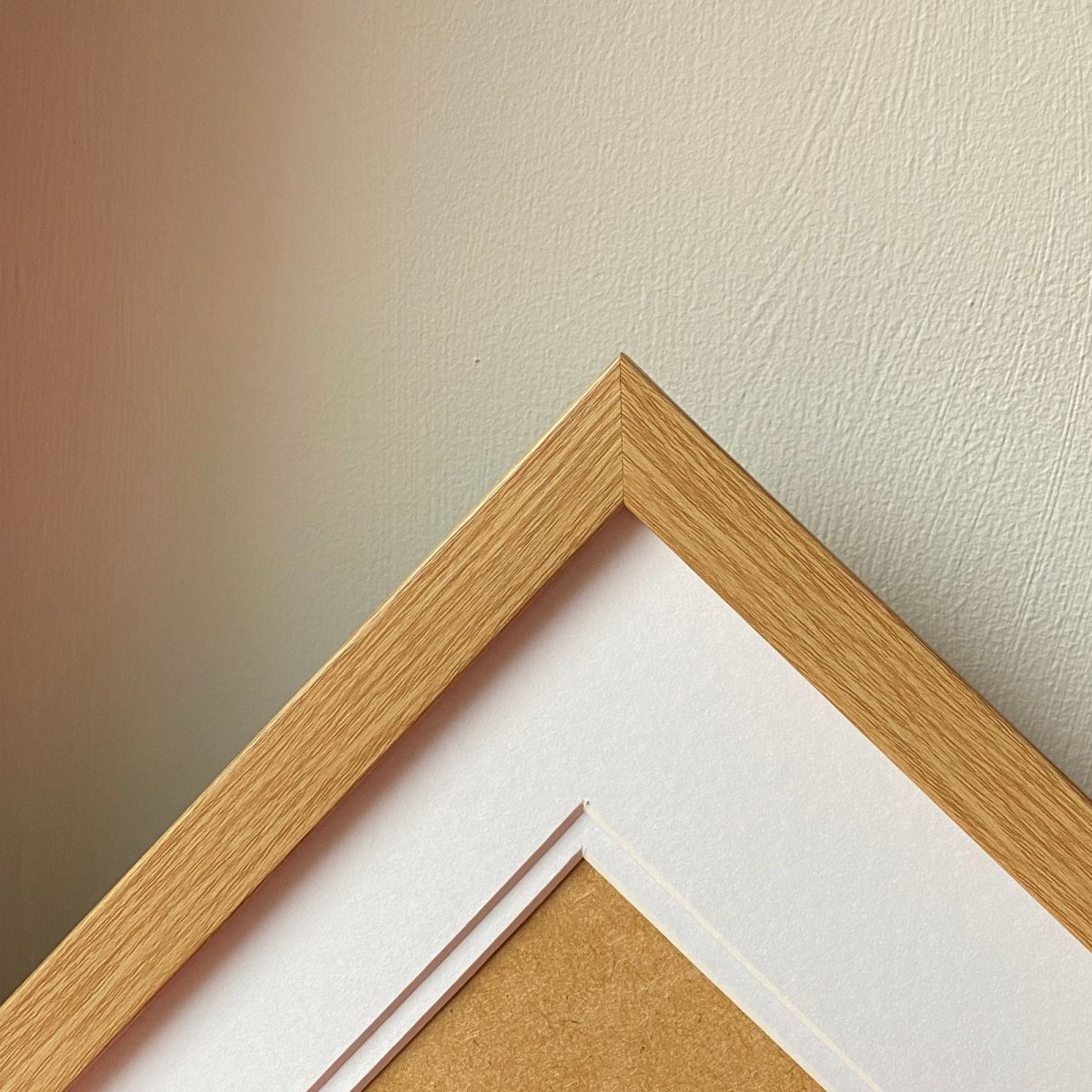 A white picture mount inside a light brown frame against a white wall