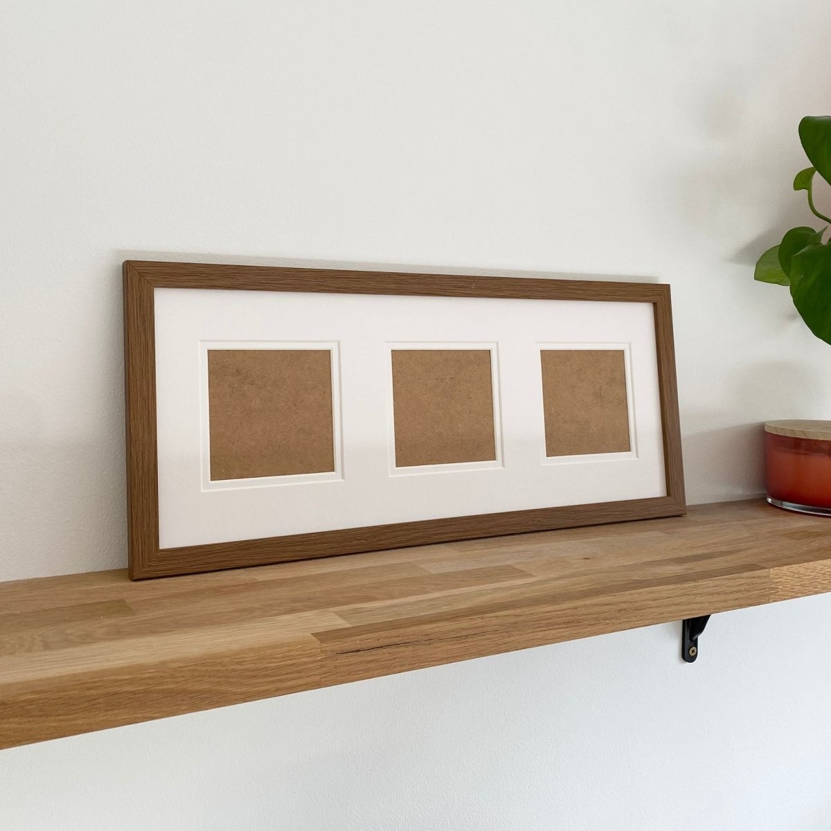 Wood-grain effect picture frame with three brown square panels on a wooden shelf against a white wall.