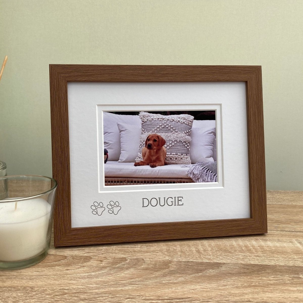 Wood-grain effect photo frame with a picture of a dog named Dougie on a wooden tabletop, with a candle in the background.