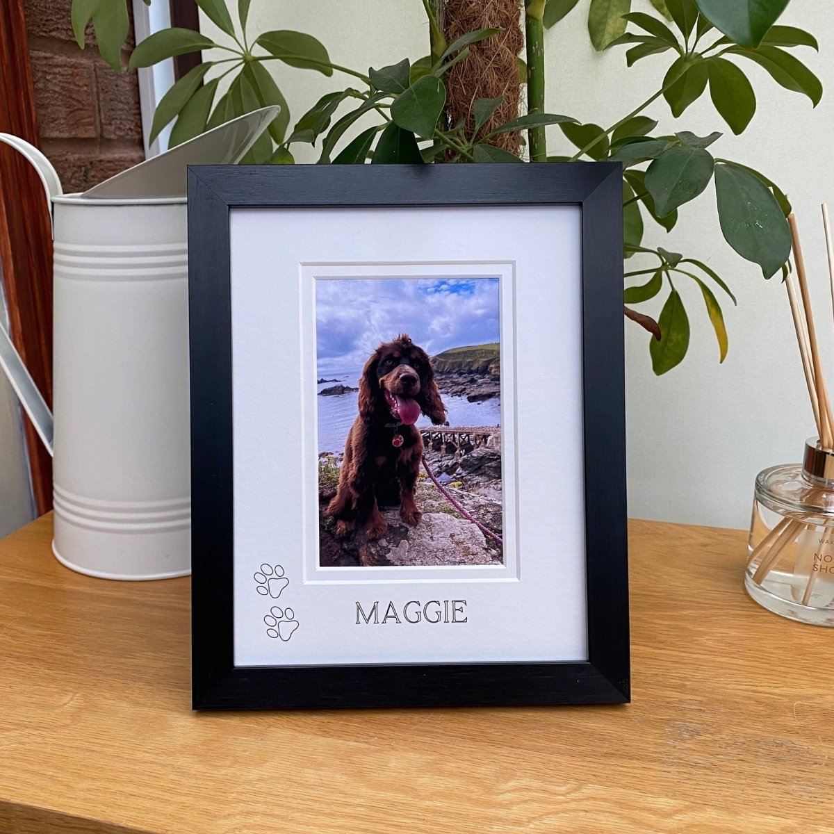 Framed photo of a dog named Maggie on a wooden surface with plants in the background