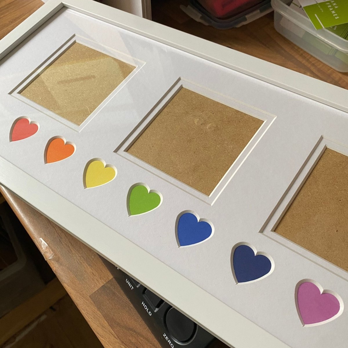 White photo frame with colorful heart cutouts on a wooden surface