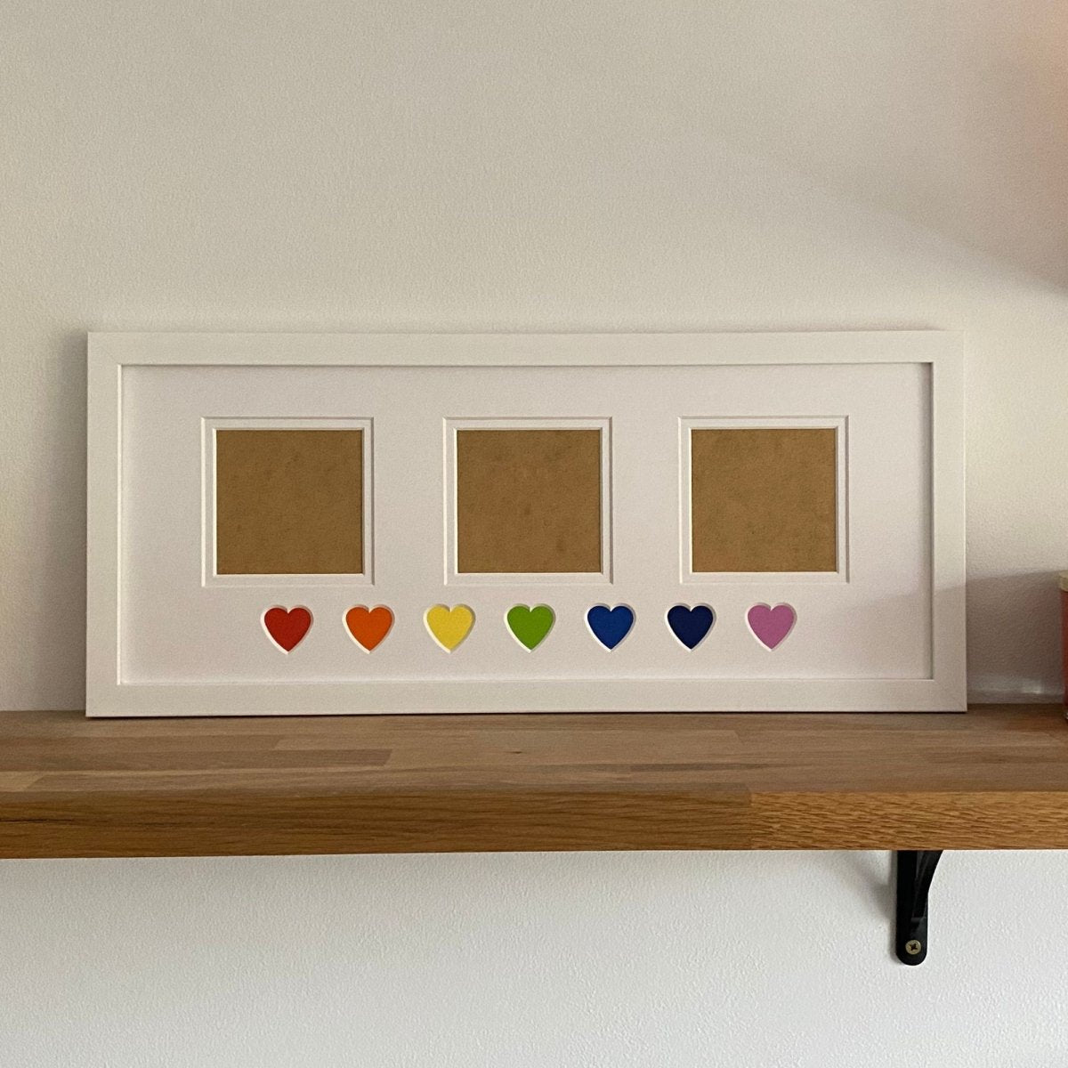Framed photo display with colored hearts on a wooden shelf against a white wall.