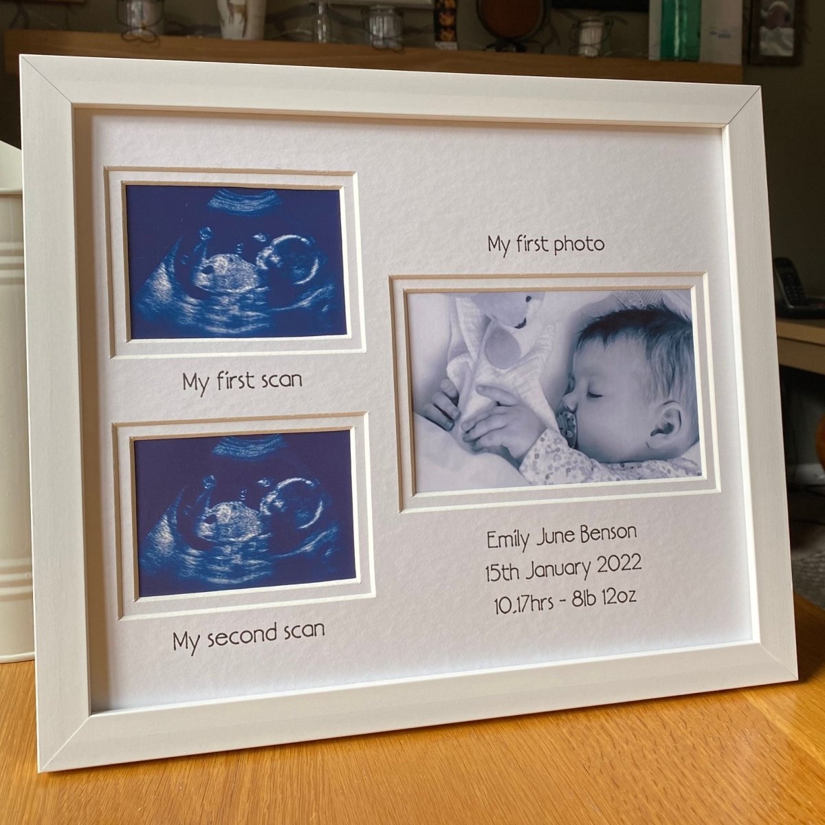 Framed baby photo album with ultrasound images and text on a wooden surface