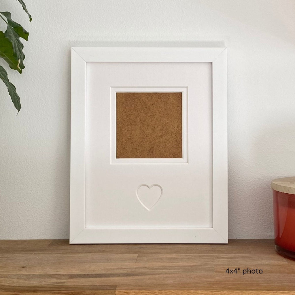 white single-aperture heart picture frame displaying family photo on wooden shelf
