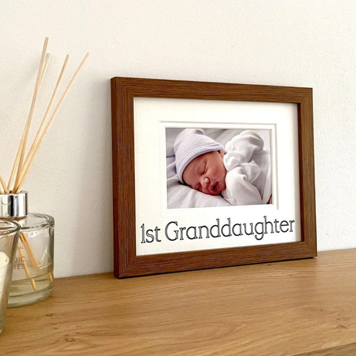 A photograph of a baby 1st Grandaughter  in a dark brown photo frame on the shelf