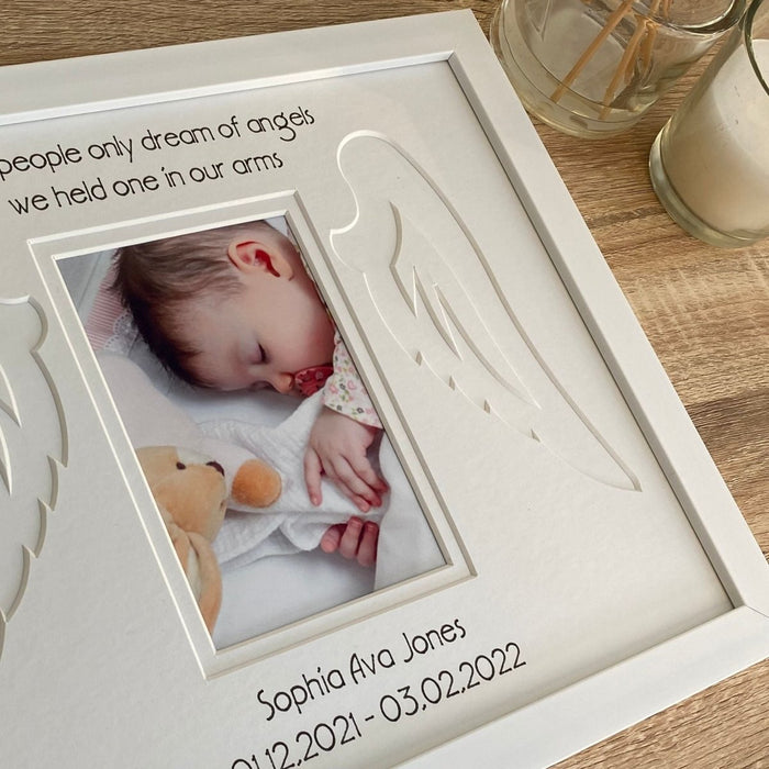 Shape of angel's wing and baby's personalisation details on the photo mount in a frame on the tabletop