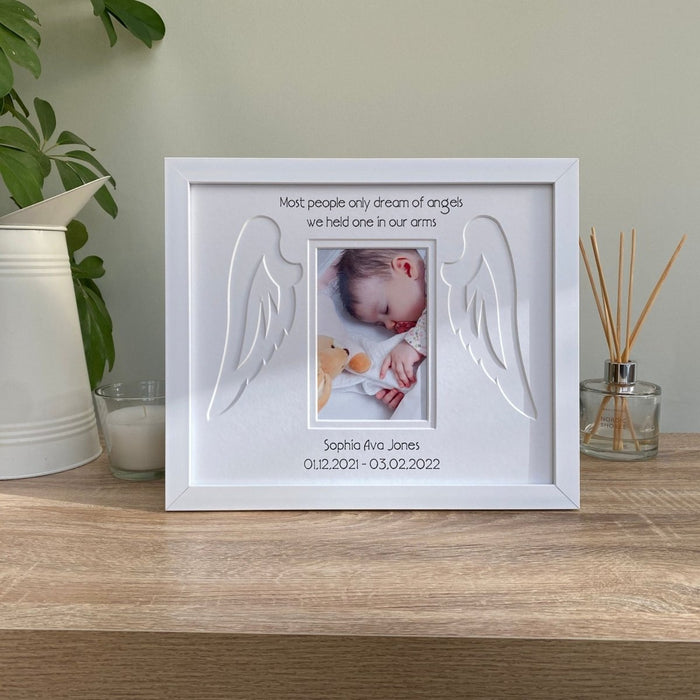 Baby Memorial white frame on the tabletop next to a candle, diffuser and green plant, jug