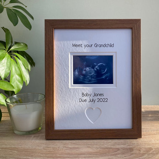 Dark brown photo frame showcasing a baby scanned image on the tabletop next to a white candle and green plant