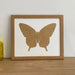 Light brown Butterfly silhouette picture frame next to a yellow glass pot against the white wall