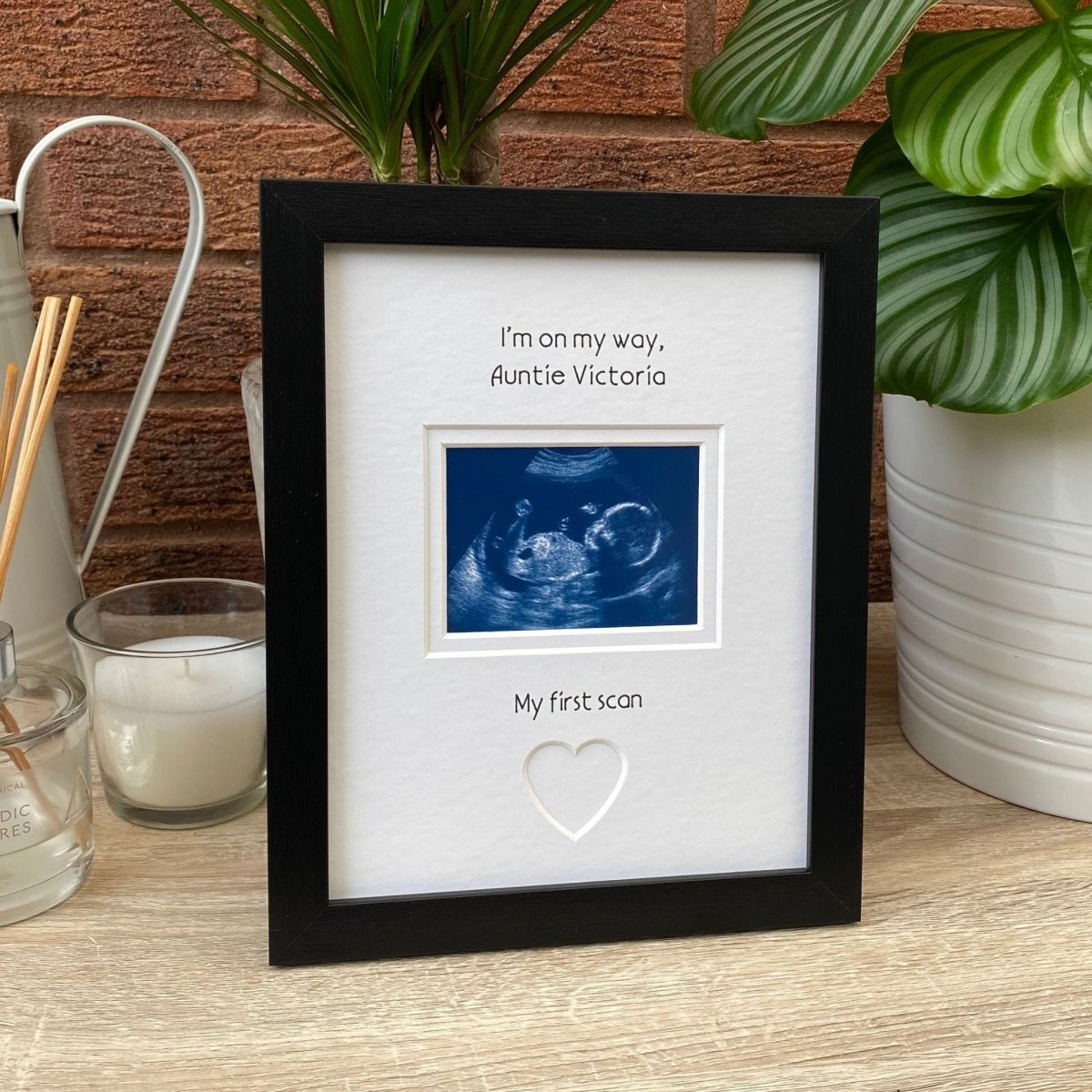 Black frame for Auntie to be, on tabletop next to a white candle, diffuser and green plant