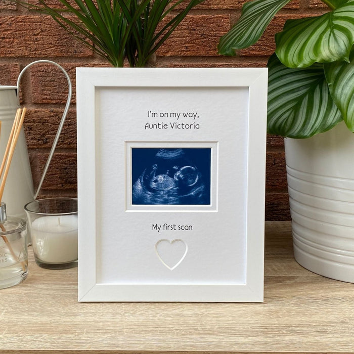 White frame, pregnancy scan image on tabletop next to a white candle and plant