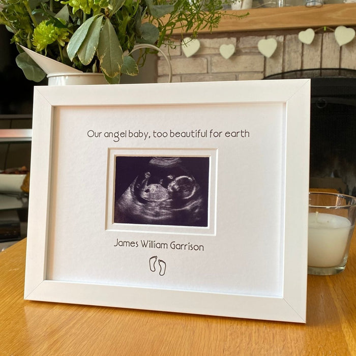 White contemporary frame, angel baby too beautiful for earth, personalisation with a feet drawing on the tabletop next to a candle and jug of fresh flowers