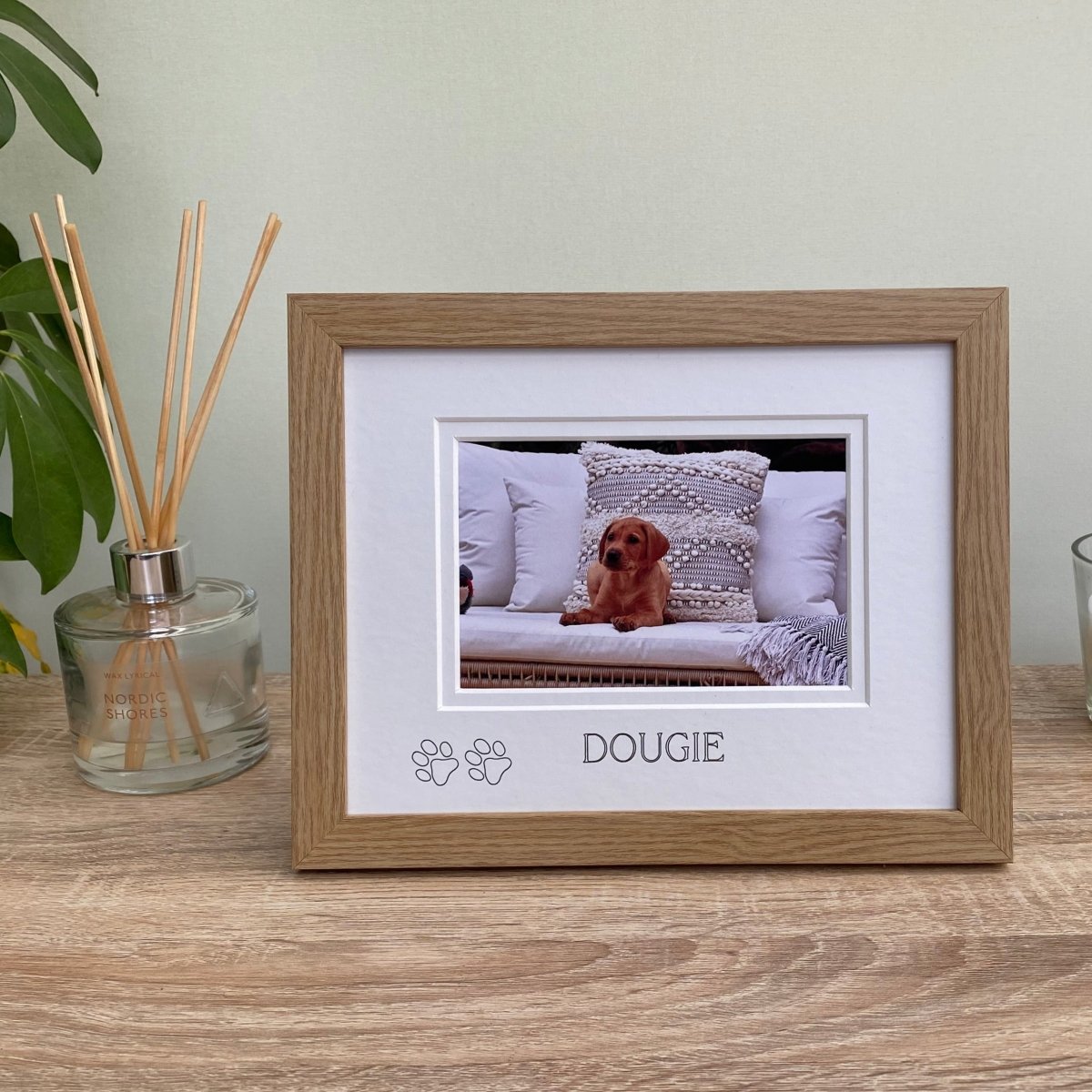 Light brown, wood-grain effect personalised puppy picture frame, freestanding on tabletop next to a white candle, diffuser and plant