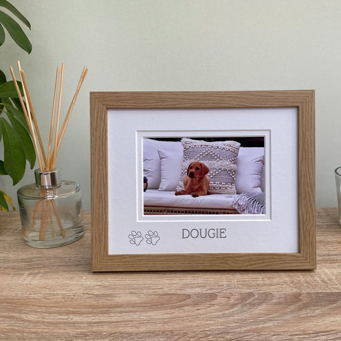 Light brown, wood-grain effect personalised puppy picture frame, freestanding on tabletop next to a white candle, diffuser and plant