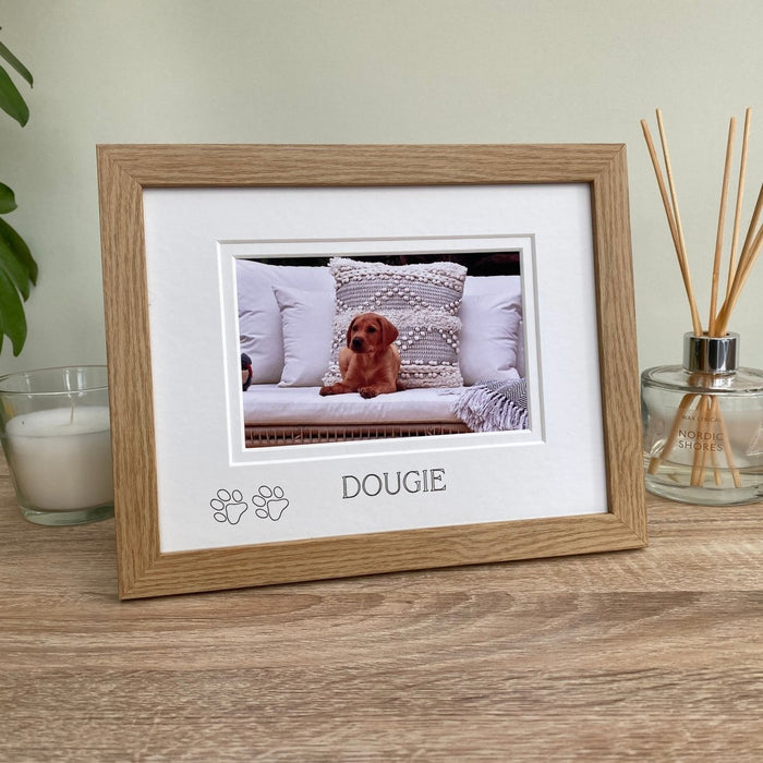 Light brown, wood-grain effect puppy picture frame, freestanding on tabletop next to a white candle, diffuser and plant