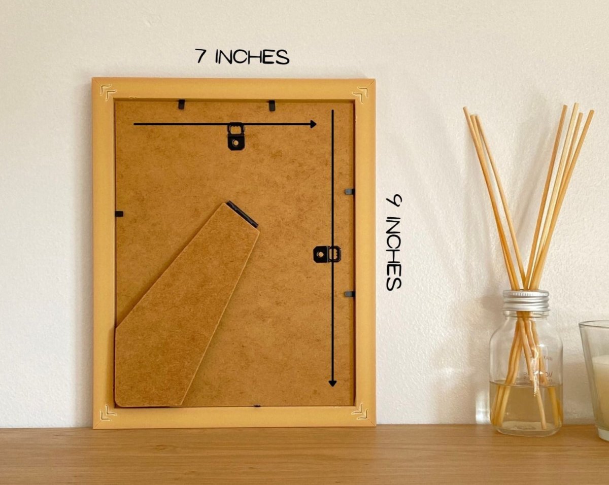 Back of a picture frame, measures 9 x 7 inches on a floating shelf next to a diffuser.