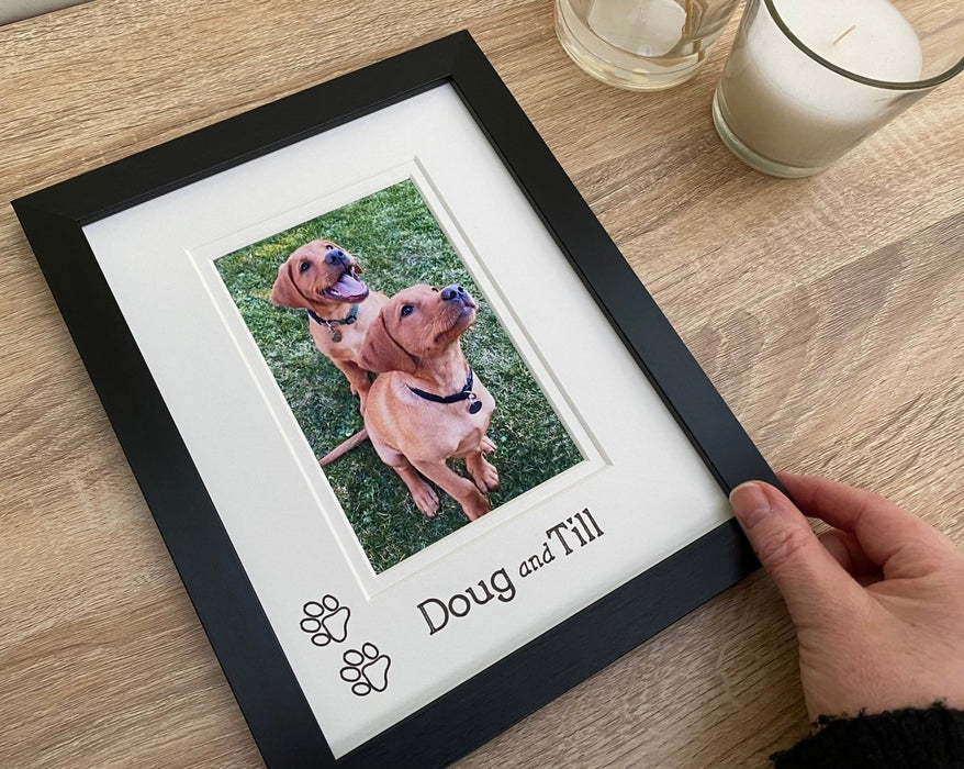 Black contemporary picture frame with an image of two fox red puppies, siblings and custom personalisation with their names. My hand holding the frame for scale purposes.