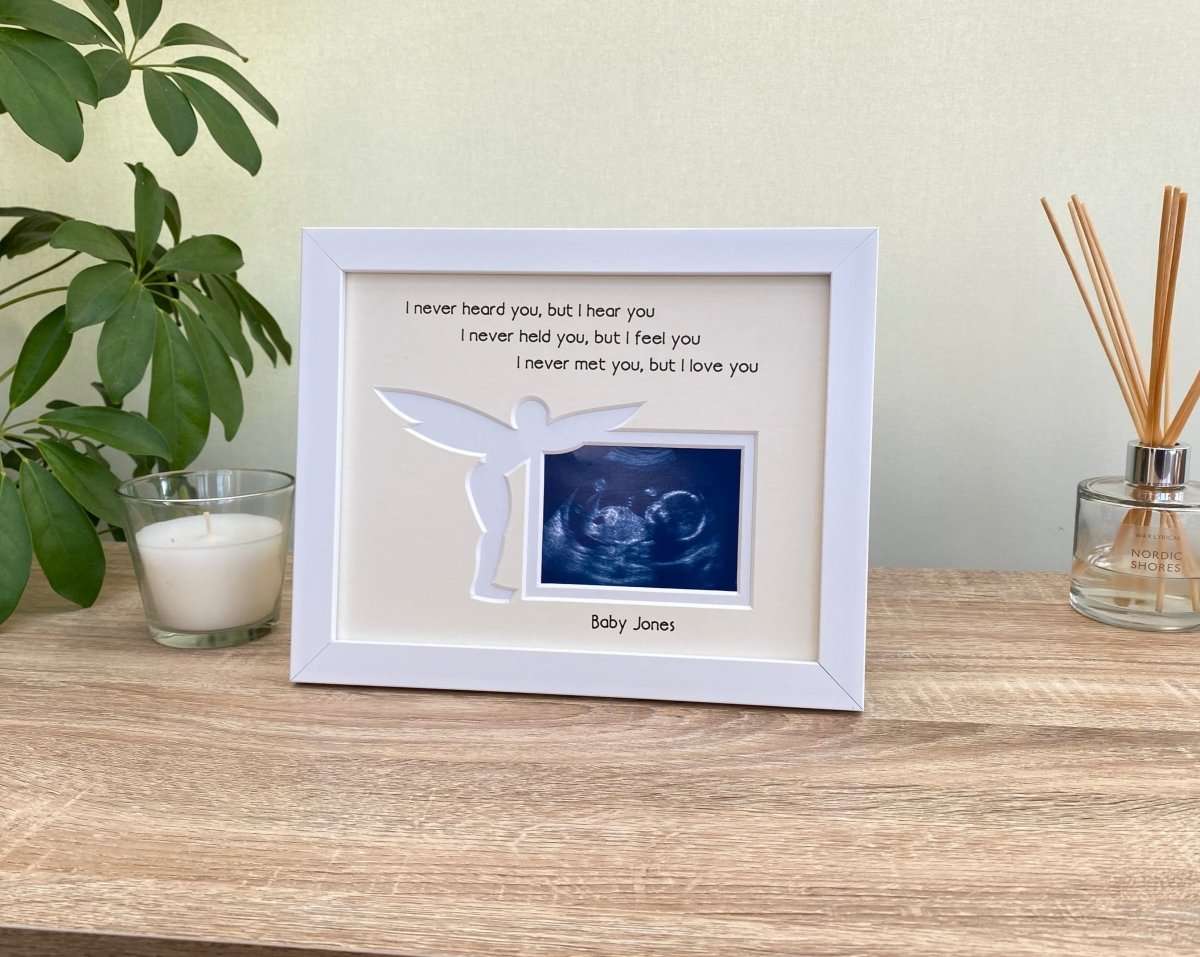 White frame with a cream double matted displaying a baby sonogram image for pregnancy loss gift, next to a white candle to light up on baby's remembrance anniversary..