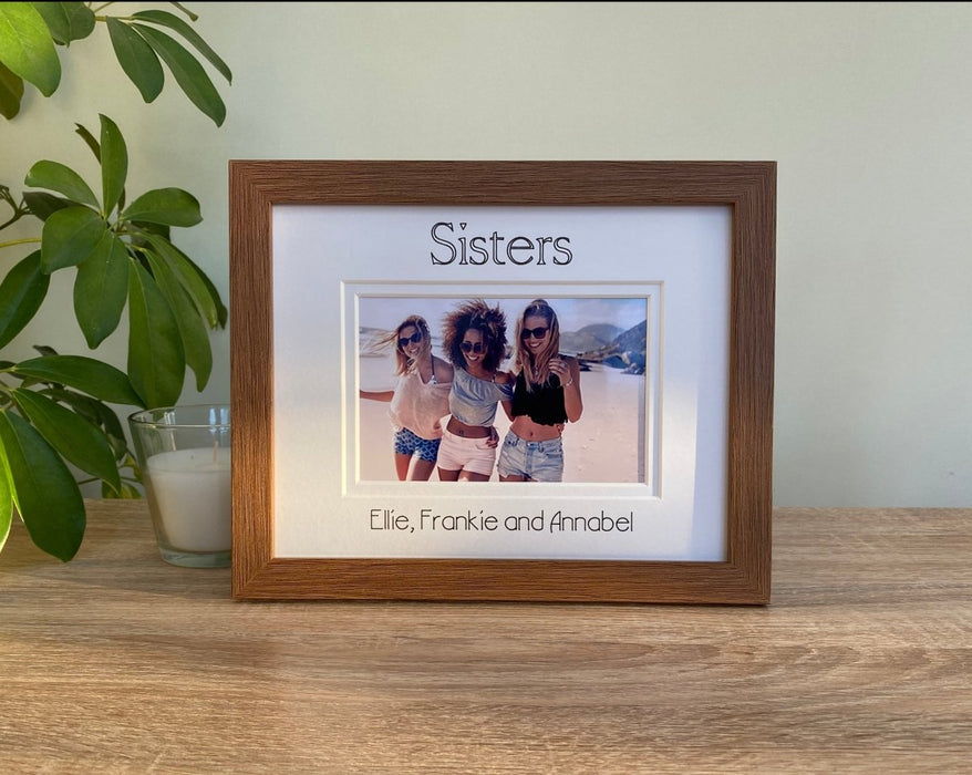 A photo of the sisters inside a brown picture frame with the personalisation, Sisters is inscribed on the top, next to a candle..