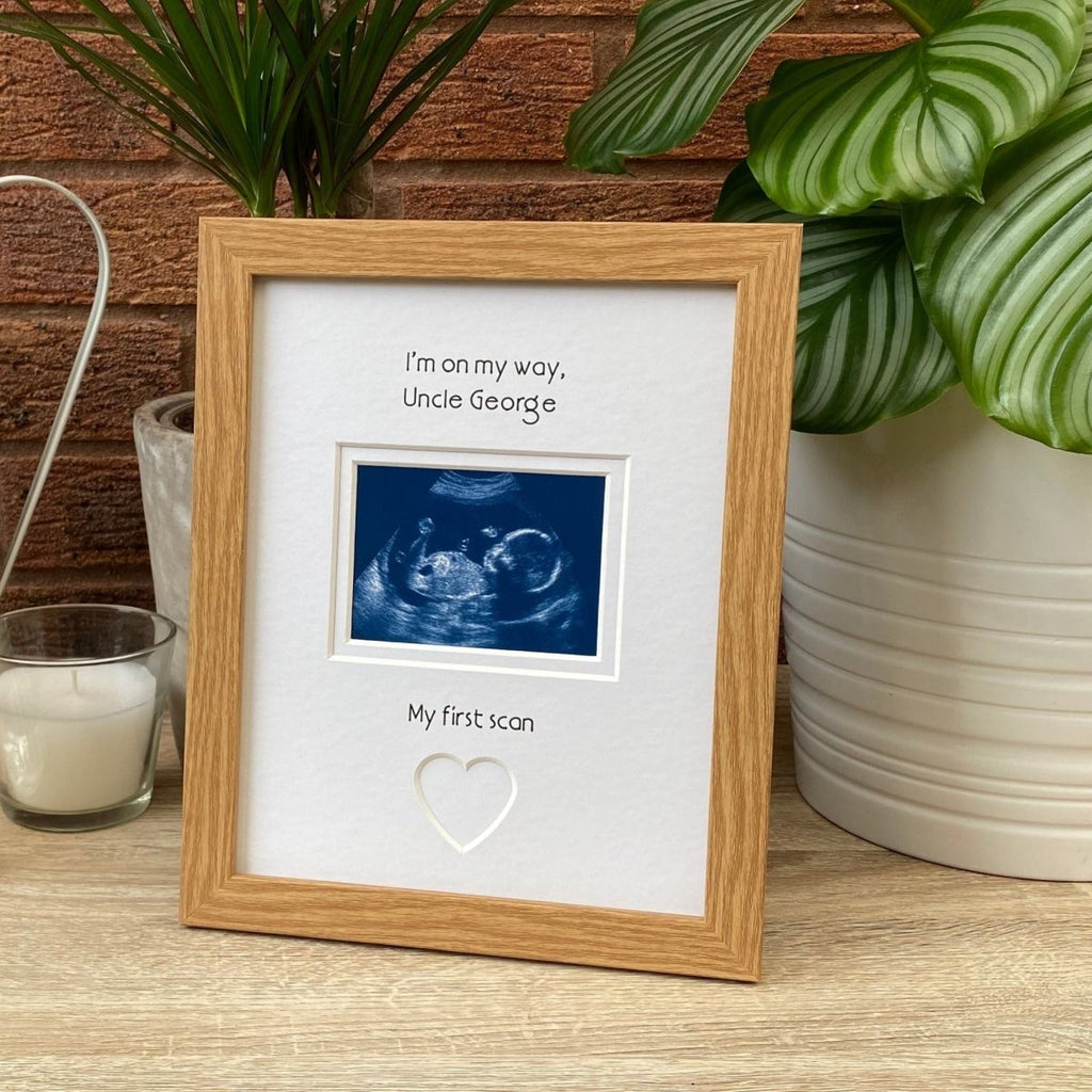 Light brown picture frame on tabletop next to a green plant and a candle