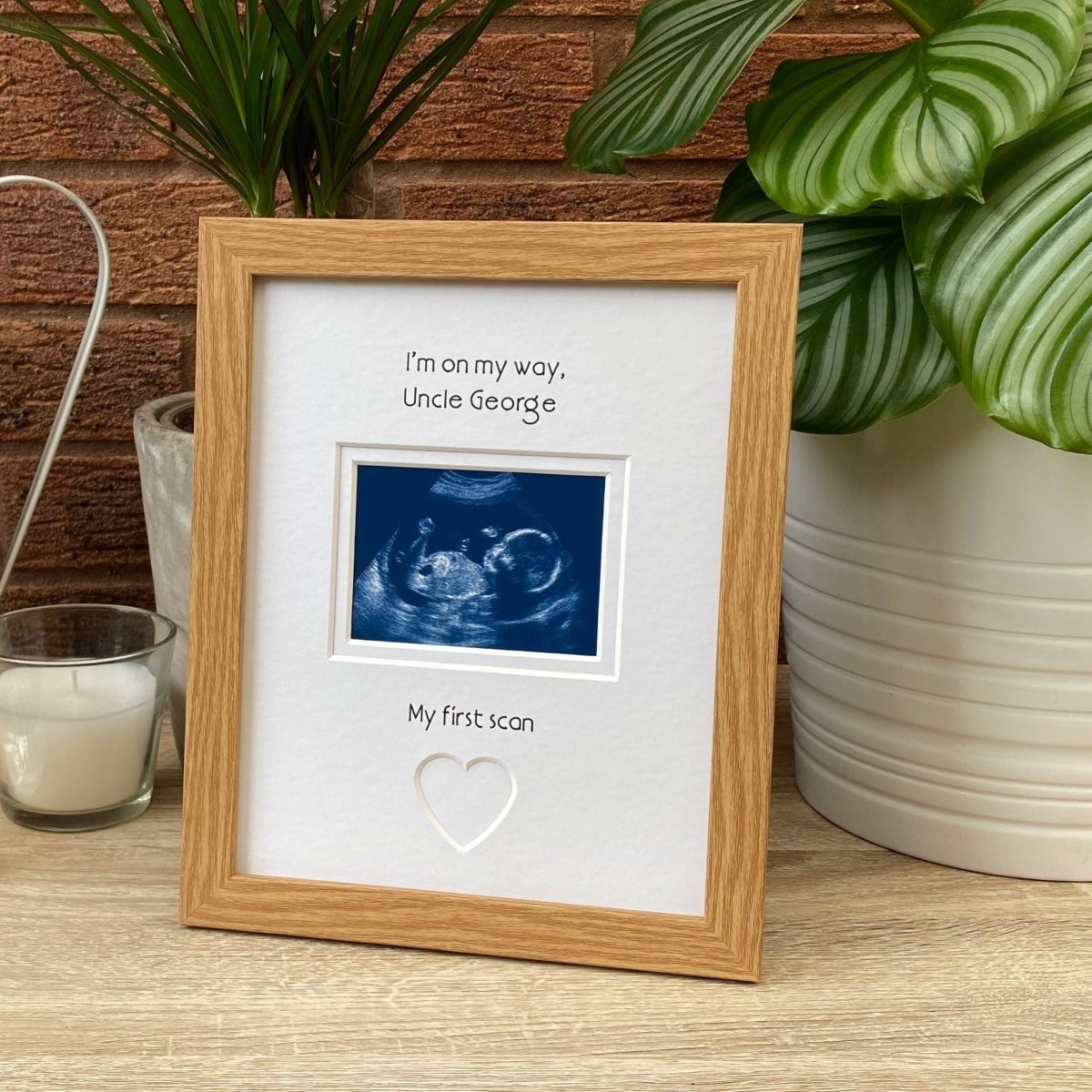 Light brown picture frame on tabletop next to a green plant and a candle