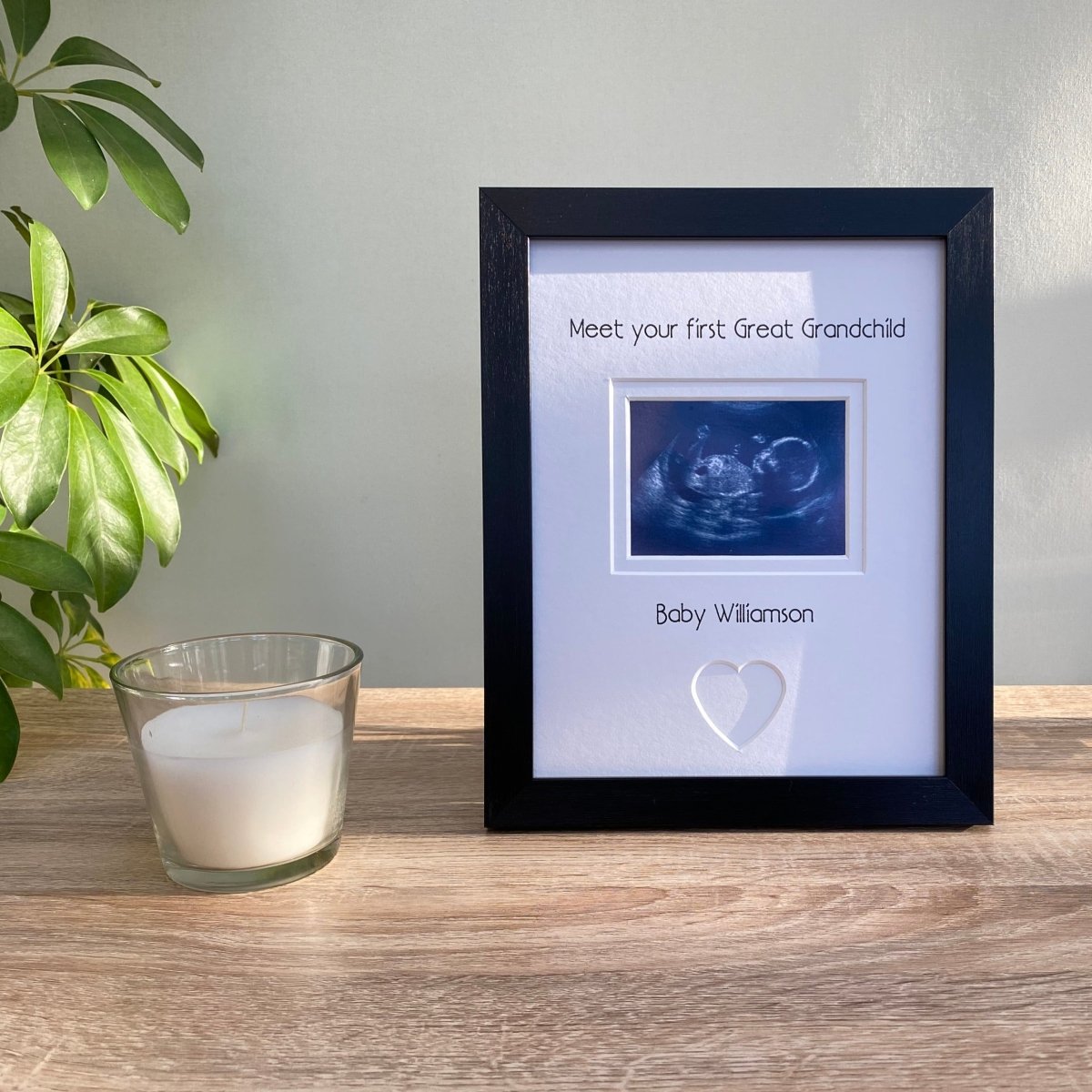 Freestanding, contemporay black picture frame, scan image of your 1st Great Grandchild with a heart shape. Next to a white candle and green plant