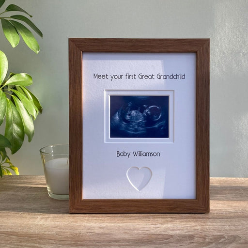 Freestanding, dark brown picture frame, scan image of 1st Great Grandchild with a heart shape. Next to a white candle and green plant