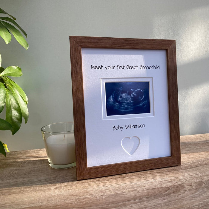 Ultrasound scan image frame of 1st Great Grandchild with a heart shape. Next to a white candle and green plant