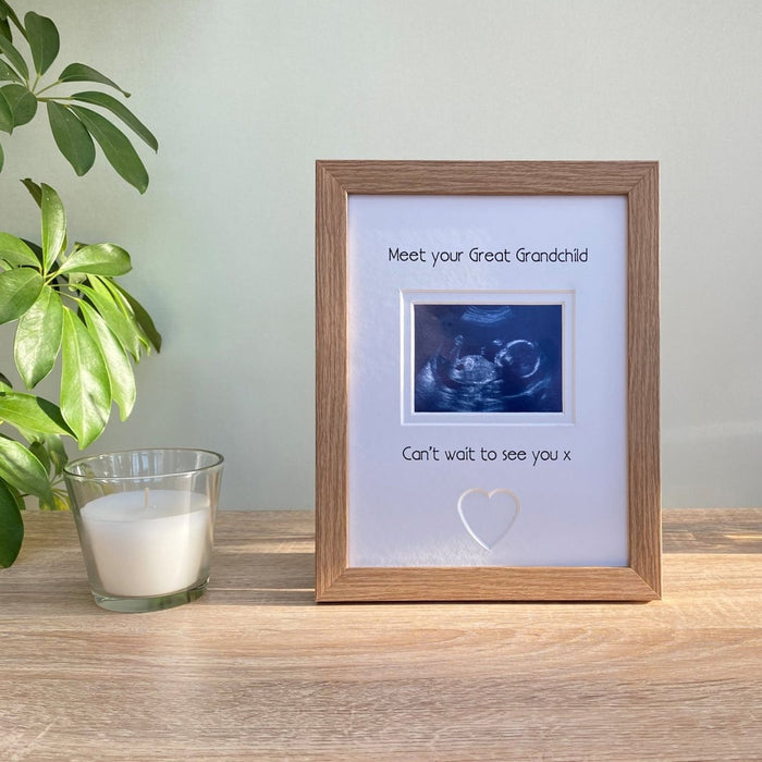 Light brown, wood-grain effect first scan picture frame next to a white candle and plant