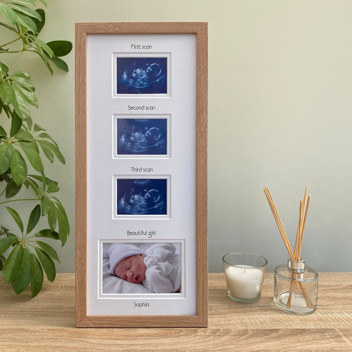 Light wood-grain brown multipicture frame on tabletop next to a plant, diffuser and candle