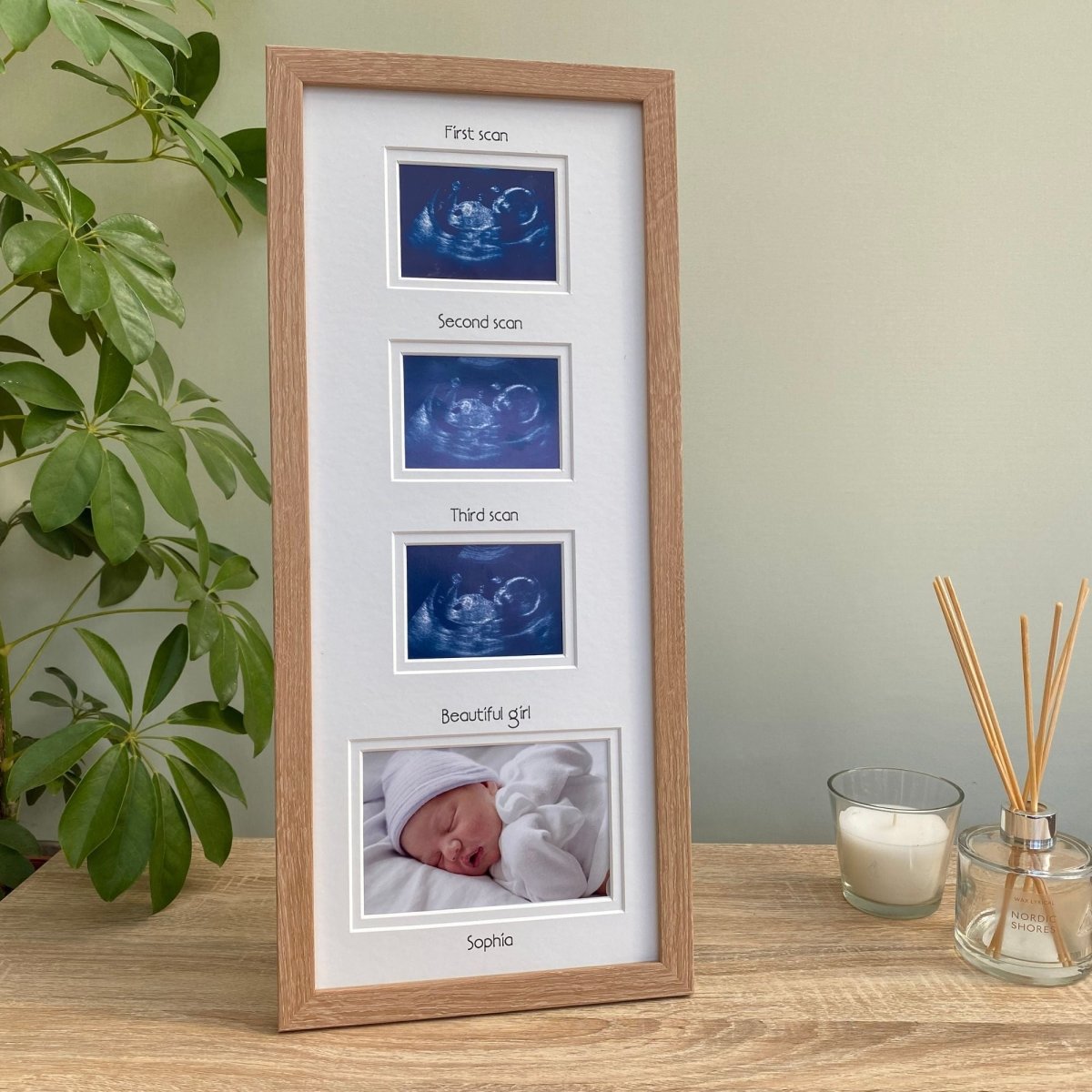 Light brown baby picture frame on tabletop next to a plant, diffuser and candle